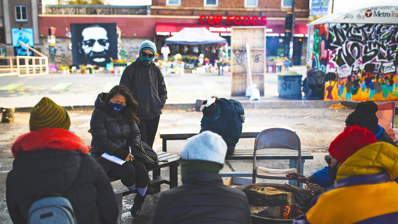 Group of people sitting, standing, and teaching, across from the George Floyd memorial space in and around Cup Foods in South Minneapolis, MN