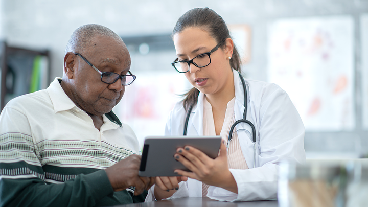 Senior man speaks with a health care provider while looking at a digital display