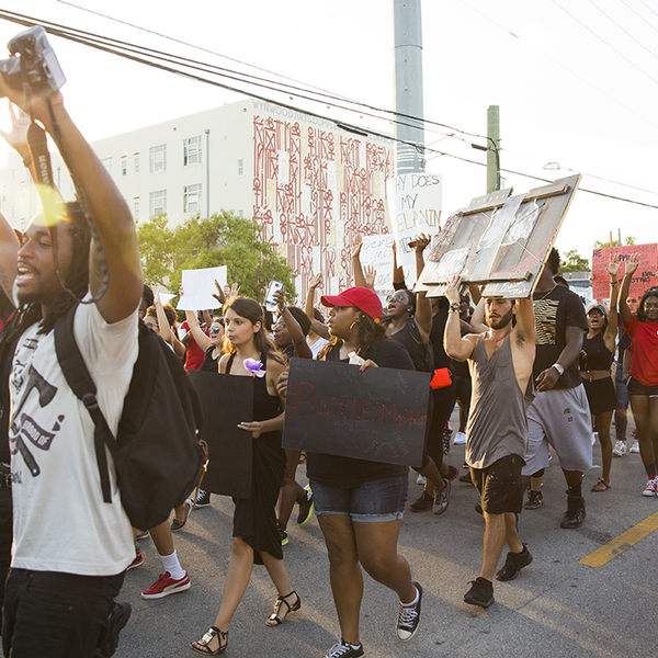 People march in protest down a street while holding signs